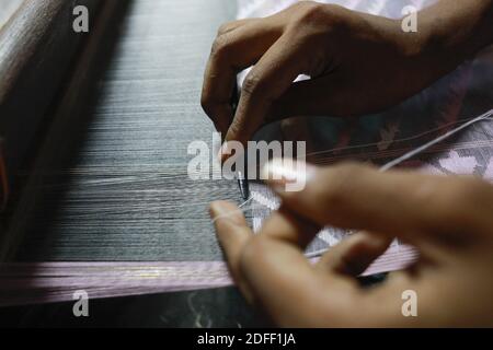 Handwebwebwebweber webt Jamdani Saree auf einem traditionellen hölzernen Handwebwebstuhl in Tarabo, nahe Dhaka, Bangladesch, 18. Juli 2020. Jamdani ist eines der feinsten Musselin-Textilien Bengalens, das seit Jahrhunderten im Dhaka District, Bangladesch, hergestellt wird. Die historische Produktion von jamdani wurde von kaiserlichen Warrants der Mogulherrscher bevormundet. Unter dem britischen Kolonialismus gingen die bengalischen Jamdani- und Musselin-Industrien aufgrund kolonialer Importpolitik, die industriell hergestellte Textilien begünstigte, rasch zurück. In den letzten Jahren hat die Produktion von Jamdani eine Wiederbelebung in Bangladesch erlebt. Das traditionelle Stockfoto