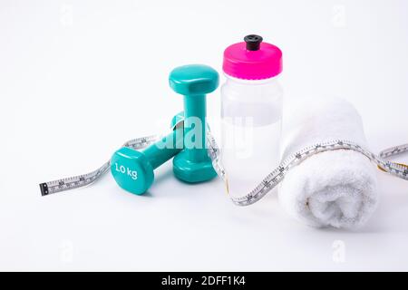 Eine Flasche Wasser, Hanteln, ein Handtuch und ein Maßband auf einer weißen Oberfläche Stockfoto