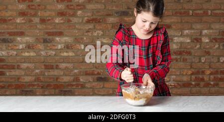 Kleines Mädchen in roten Tartan Kleid Mischen Teig Stockfoto