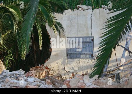 Die letzten Überreste eines alten verletzten Gebäudes in der Landschaft der Costa Blanca, Spanien. Nur eine Wand bleibt mit einem Paar blauer Fensterläden. Stockfoto