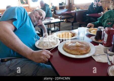 Mann konfrontiert sein riesiges Frühstück mit Pfannkuchen, Rührei, Kartoffelrösti und Grütze im Twin Gable Cafe am Straßenrand. Brule Wisconsin WI USA Stockfoto