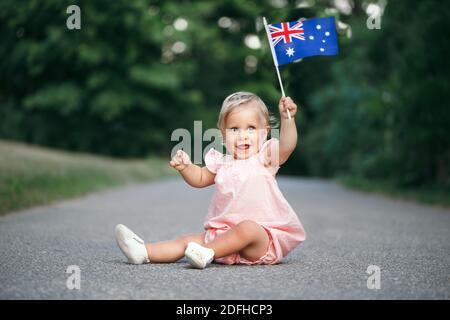 Niedlich liebenswert kaukasischen Baby Mädchen winkt australische Flagge. Lächelndes Kind, das auf der Straße im Park sitzt und den Australia Day feiert. Feiern Stockfoto