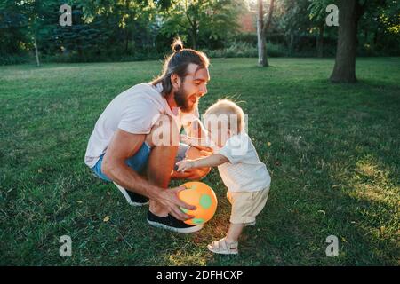 Vatertag. Vater spielt Ball mit Kleinkind Baby Junge im Freien. Elternteil verbringt Zeit zusammen mit Kind Sohn im Park. Authentischer Lifestyle-Moment Stockfoto