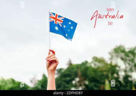 Happy Australia Day Karte mit Grußtext. Nahaufnahme einer Frau mit menschlicher Hand, die die australische Flagge gegen den blauen Himmel schwenkt. Stolzer Bürgermann feiert Stockfoto