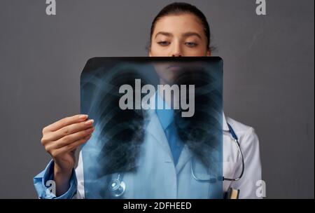 Eine Frau in einem medizinischen Kleid untersucht Röntgenstrahlen auf einem Grauer Hintergrund Stockfoto