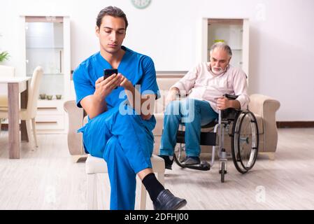 Alter Mann im Rollstuhl und schlechter Betreuer drinnen Stockfoto