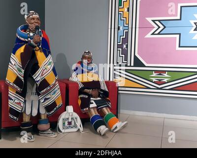 Johannesburg, Südafrika. November 2020. In traditioneller Tracht spricht die südafrikanische Künstlerin Esther Mahlangu (l.) neben einem Verwandten in einer Galerie, in der Mahlangs Kunstwerke ausgestellt sind. Der 85-jährige Künstler gehört zum Stamm der Ndebele, der vor allem im Norden Südafrikas beheimatet ist. (To dpa from Tradition to world Fame: South African artist Esther Mahlangu) Credit: Kate Bartlett/dpa/Alamy Live News Stockfoto