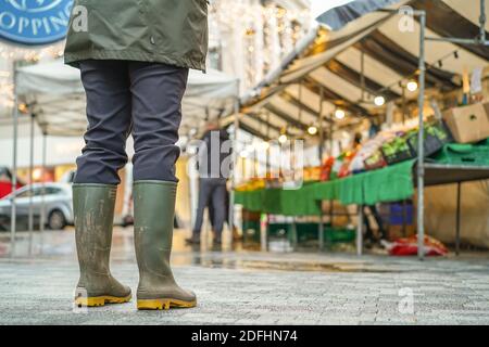 Kidderminster, Großbritannien. Dezember 2020. Am ersten Weihnachts-Shopping-Wochenende nach Lockdown zwei Einschränkungen aufgehoben sind, sieht frühmorgendlichen Markt Händler ihre Stände für, was sie hoffen, wird ein geschäftiger festlicher Handelstag. Da die Käufer erwartet werden, dass sie in Kraft sind, sind öffentliche Warnschilder in der Stadt vorhanden, die die Menschen an wesentliche soziale Distanzierungsmaßnahmen erinnern. Eine Kundin im Winter wellington Stiefel wird hier gesehen, hält ihre Distanz, wartet geduldig auf den Obst & Gemüse Stand zu öffnen. Kredit: Lee Hudson/Alamy Live Nachrichten Stockfoto