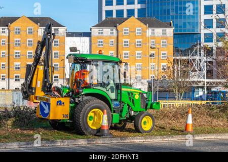 Ein Traktor mit Heckenschneidevorrichtung, der am Straßenrand arbeitet, um die Vegetation zurückzuschneiden und Wartungsarbeiten auf der Autobahn durchzuführen. Stockfoto