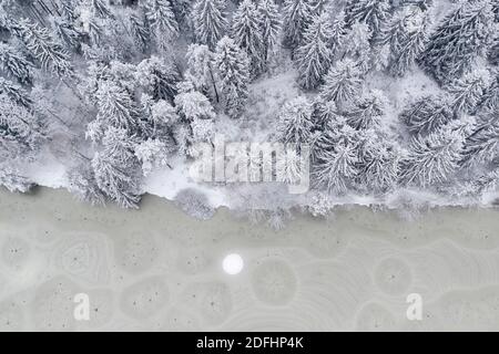 Eine Luftdrohne, die nach unten schaut, fängt Muster, Formen, Löcher und Risse in gefrorenem Seeis ein. Stockfoto