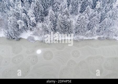 Eine Luftdrohne, die nach unten schaut, fängt Muster, Formen, Löcher und Risse in gefrorenem Seeis ein. Stockfoto