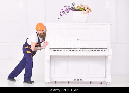 Mover Stirnrunzeln während bewegen schweren Klavier. Müde bärtige Mann Umzug Sachen in der Wohnung isoliert auf weißem Hintergrund. Haus Redecoration Konzept. Stockfoto