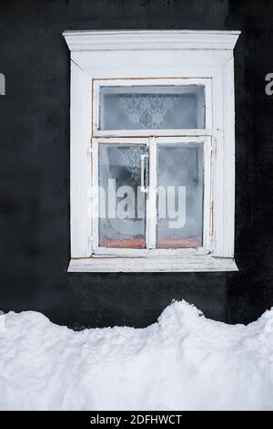 Die Schneeverwehung unter dem gefrorenen Holzfenster mit Thermometer Das alte Landhausgebäude im Wintertag Stockfoto