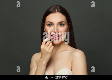 Schöne Frau, die roten Lippenstift auf den Lippen auf schwarzem Hintergrund Stockfoto