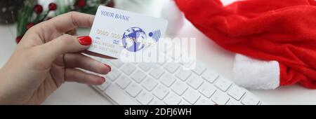 Weibliche Hände halten Bankkreditkarte in der Nähe der Tastatur und weihnachtsmann Hut und weihnachtsbaum. Stockfoto