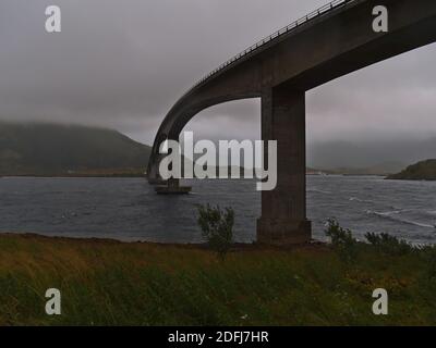 Blick auf die Freischwinger Straßenbrücke Gimsøystraumen Bru bei stürmischen Wetterbedingungen mit niedrigen Wolken und starkem Wind im Spätsommer auf den Lofoten-Inseln. Stockfoto