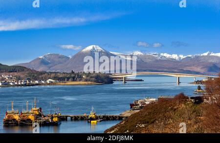 SKYE BRÜCKE MIT SCHNEEBEDECKTEN CUILLIN HÜGELN UND EILEAN VERBOT [WEISSE INSEL] MIT HÄUSERN DES KLEINEN DORFES KYLEAKIN Stockfoto