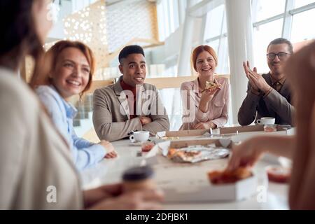 Eine Gruppe von Mitarbeitern in einer Pause genießen chatt und Essen in einer fröhlichen Atmosphäre in der Firmenkantine. Menschen, Arbeit, Unternehmen, Geschäftskonzept. Stockfoto