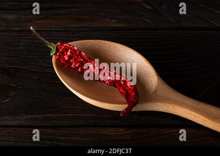 Trockene Schote von rotem Chili in einem großen Holzlöffel auf einem schwarzen Holztisch Nahaufnahme. Natürliche Gewürze und Gewürze für Fleisch, Fisch und Gemüse. Stockfoto