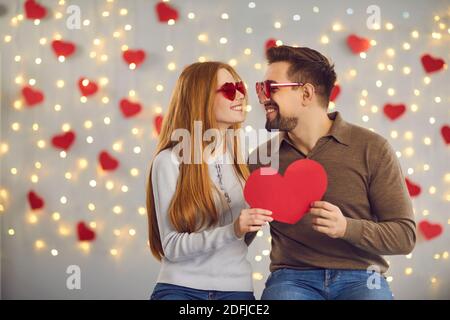 Glücklicher junger Mann und Frau halten Valentine-Karte, Blick auf einander und lächelnd Stockfoto