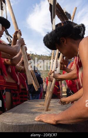 Naga-Männer, die im Dorf Kisama mit Holzstäben Körner mahlen Am 2. Dezember 2016 in Nagaland, Indien Stockfoto