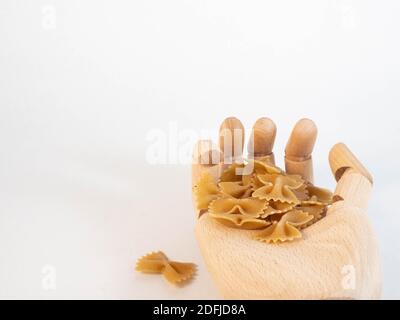 Eine hölzerne Hand, die eine Handvoll Farfalle Teig hält. Konzept rund um Essen und Konsum. Stockfoto