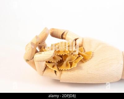 Eine hölzerne Hand, die eine Handvoll Farfalle Teig hält. Konzept rund um Essen und Konsum. Stockfoto