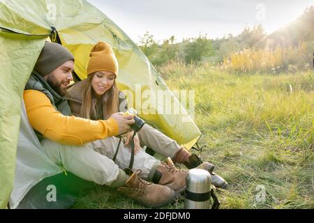 Junger Mann, der seiner hübschen Frau Fotos in Fotokamera zeigt Während der Erholung im Zelt in natürlicher Umgebung im Herbst Wochenende während der Reise Stockfoto