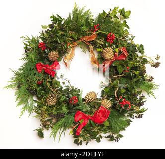 Isolierter festlicher Weihnachtskranz aus Efeu, Stechpalme, Nadelbaum, Tannenzapfen und Bändern. Stockfoto