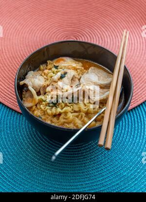 Eiernudeln mit Schweinefleisch, Spiegelei, Gemüse und Suppen in Schüssel und Essstäbchen mit Löffel kochen. Thailändische Nudelsuppe, selektiver Fokus. Stockfoto