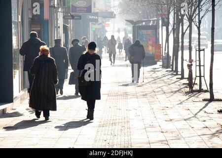 Belgrad, Serbien - 1. Dezember 2020: Eine Frau, die allein auf dem belebten Bürgersteig der Stadt an einem sonnigen, kalten Herbsttag geht Stockfoto