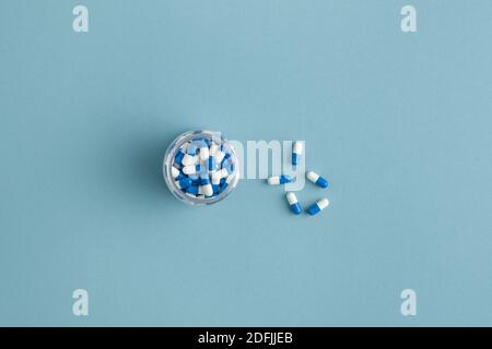 Flaches Layout von mehreren Mulsi-Farbe medizinischen Kapseln mit der gleichen Pillen in kleinen Glas oder Flasche in der Nähe in Isolation Vor staubblauem Hintergrund Stockfoto