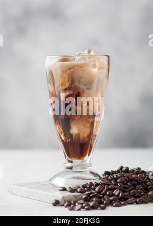 Hohes Glas Eiskaffee mit Milch mit frischen rohen Kaffeebohnen auf hellem Tischhintergrund. Stockfoto
