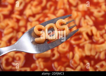 Spaghetti-Buchstaben Schreibweise das Wort SOS steht für Save our Souls, mit den Buchstaben auf einer Gabel gehalten, dahinter ist die rote Tomatensauce. Stockfoto