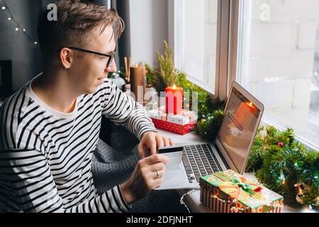 Mann Kunde hält Kreditkarte Online-Shopping Zahlung im Internet-Shop zu Hause. Weihnachten Geschenk-Box Dekoration, Neujahr Winter Verkauf, Weihnachten d Stockfoto