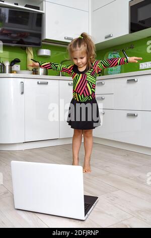 Kleines Mädchen mit Laptop macht Gymnastik zu Hause Stockfoto