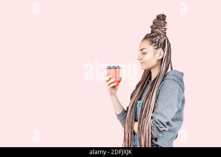 Schöne moderne junge Frau mit rosa Zöpfen sieht verliebt in Papier Einweg-Tasse mit Tee. Konzept für Werbegetränke Kaffee zum Mitnehmen, Mitnehmen Stockfoto