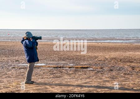 Frau, die an einem hellen, aber kalten Wintertag Vögel am östlichen Ufer des Wash fotografiert. Stockfoto