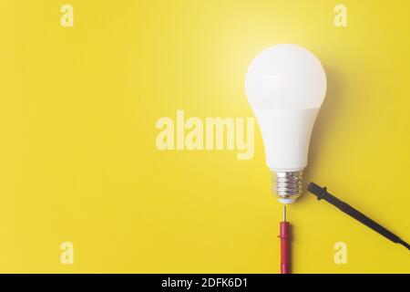 Glühlampe mit Multimetersonden auf gelbem Hintergrund, einzigartiges Konzept. Idee, Innovation, Kreativität Konzept, Design-Vorlage, Kopierraum Stockfoto