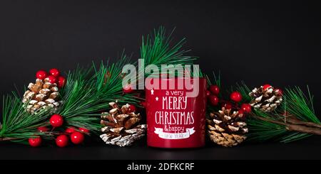 Weihnachtliche Stillleben mit roter Kerze und Tannenzweigen mit Tannenzapfen und Stechbeeren auf dunklem Grund. Weihnachtskarte mit Wünschen von einem Merry Chri Stockfoto