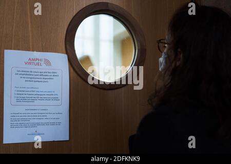 Eine Frau schaut durch ein Fenster neben einem Schild mit der Aufschrift "virtuelles Amphitheater", während die Klasse für andere Studenten in einem Amphitheater an der Universität La Sorbonne, Rue du Pantheon, in Paris, Frankreich, am 13. Oktober 2020 vermittelt wird. Eine der größten öffentlichen Universitäten Frankreichs ist fest davon überzeugt, dass sie auf dem Campus keine "physische Distanz" aufzwingen wird, sondern sagt, dass sie die Bemühungen zum Schutz von Mitarbeitern und Studenten vor COVID-19 verstärkt hat. An der Universität Pantheon-Sorbonne wurden Handdesinfektionsdispenser installiert, wiederverwendbare Masken sind sofort verfügbar und der Zeitpunkt der Kurse wurde im Rahmen neuer Maßnahmen versetzt Stockfoto