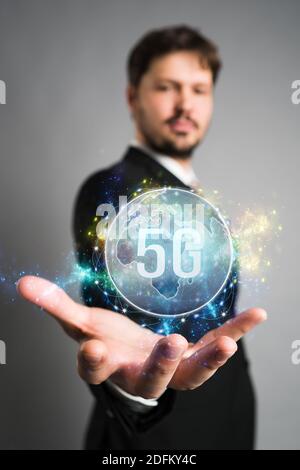 Geschäftsmann präsentiert eine virtuelle Weltkarte mit Nachricht 5G in Vorderseite mit grauem Hintergrund Stockfoto