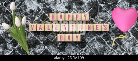 Würfel mit Nachricht GLÜCKLICH VALENTINSTAG und romantische Dekoration auf Lavastein Hintergrund Stockfoto