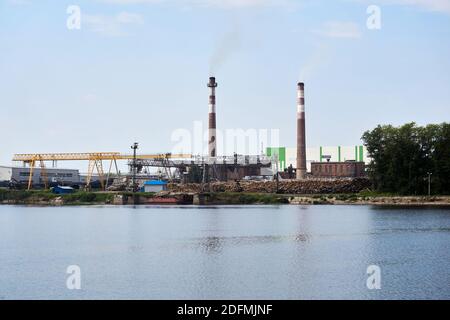 Industrielandschaft, Zellstoff- und Papierfabrik mit Holzstapeln und Kaminen am Fluss Stockfoto