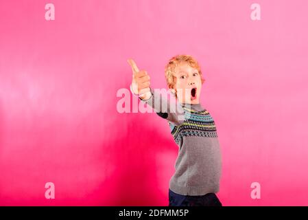 Junge Kleinkind Junge trägt Winterpullover tun den Daumen nach oben Zeichen isoliert auf einem Studio Hintergrund. Stockfoto