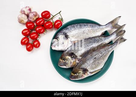 Roher dorado Fisch auf grünem Teller auf weißem Tisch. Draufsicht, Kopierbereich Stockfoto