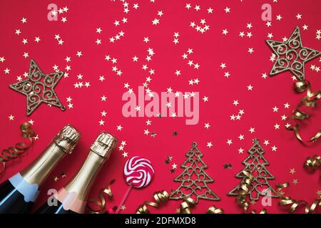 Zwei Champagnerflaschen, Weihnachtsschmuck, Cany, Konfetti-Sterne und Party-Streamer auf rotem Hintergrund. Weihnachtshintergrund, Draufsicht, Kopierbereich. Stockfoto