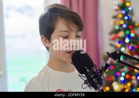 Ein Junge, der in ein Mikrofon singt, nimmt Gesang für ein Lied auf. Stockfoto