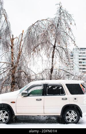 Weißes Auto bedeckt mit Eis und Schnee nach eisigen Regen. Eissturmzyklon. Stadt im Winter. Frostiges Wetter. Winterverschneite Szenen. Stockfoto