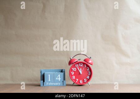 Holzwürfelförmiger Kalender für Februar 14 mit roter Uhr auf Holzhintergrund, Retro-Wecker mit fünf Minuten bis zwölf Uhr. Speicherplatz kopieren. Stockfoto